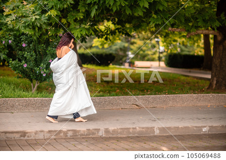 Woman city blanket. Morning in the big city. A blonde woman in a white blanket is enjoying in the city center. Photographed for social media Woman city blanket. Morning in the big city. A blonde woman in a white blanket is enjoying in the city center. Photographed for social media 105069488