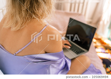 A top view of a woman in a purple nightgown using a laptop on a bed, suggesting that she is working or studying from the comfort of her own home. 105069494