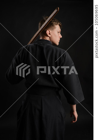 Kendo guru wearing in a traditional japanese kimono is practicing martial art with the shinai bamboo sword against a black studio background. 105069695