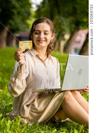 Woman using credit bank card and laptop, transferring money, purchases online shopping in city park Woman using credit bank card and laptop, transferring money, purchases online shopping in city park 105069783