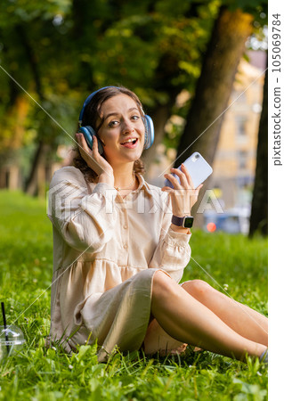 Happy young woman in wireless headphones choosing, listening music in smartphone dancing outdoors 105069784