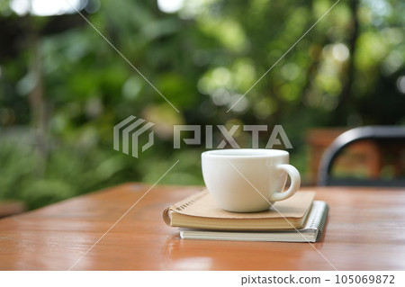 White coffee cup and bronze spoon on brown wooden table with green lush background 105069872