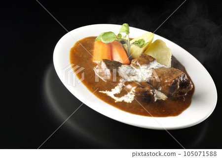 Hot beef stew with watercress, carrot, potato garnish and thick-sliced beef tongue covered with fresh cream, photographed against a black background 105071588