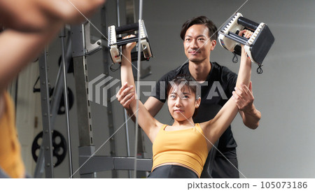 Woman training in gym and trainer supporting her Woman training in gym and trainer supporting her 105073186