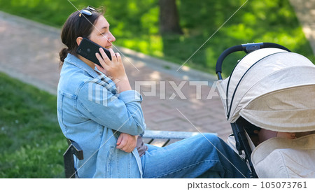 Brunette woman talks with friend on smartphone in park 105073761