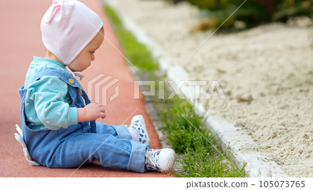 Toddler sitting on sidewalk tears grass planted near curb 105073765