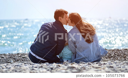 Wife and husband sitting on pebble beach kiss each other 105073766