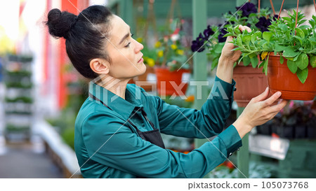 Young woman smells pot-plants hanging on shelf in store Young woman smells pot-plants hanging on shelf in store 105073768