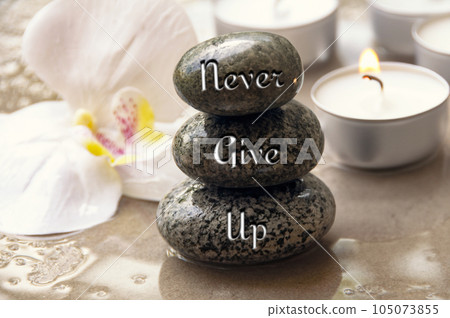 Never give up text engraved on black zen stones with orchid and candle background 105073855