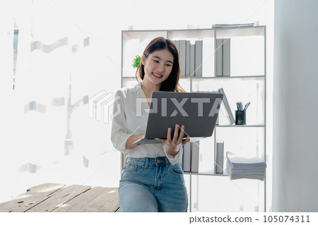 Young asian businesswoman manager, lawyer or company employee holding accounting bookkeeping documents checking financial data or marketing report working in office with laptop. Paperwork management. 105074311