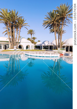 Pool and palm trees with traditional building with dome roof, Tunisia 105074394