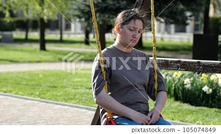Adult woman riding swing sits with upset expression in park Adult woman riding swing sits with upset expression in park 105074849