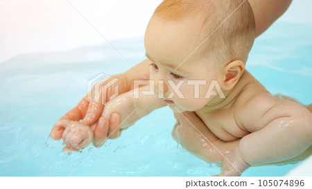 Baby girl swims in bathtub with swim teacher assistance Baby girl swims in bathtub with swim teacher assistance 105074896