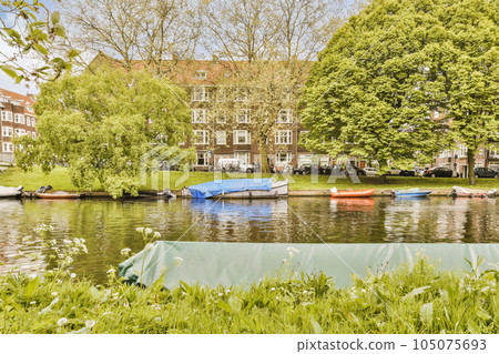 boats on the water in front of an apartment building with trees and grass around it is clear blue sky above 105075693