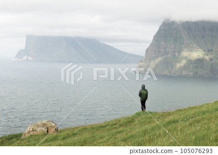 Lonely tourist near small lake looks at foggy islands in Atlantic ocean 105076293