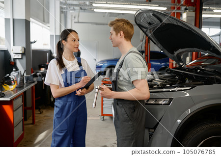 Man technician and woman mechanic talking at car service garage Man technician and woman mechanic talking at car service garage 105076785