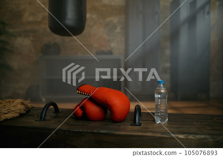 Boxing red gloves, plastic bottle of water and punching bag at sport gym 105076893