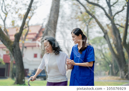 woman physiotherapist is holding a female elderly patient walking in a park to strengthen her leg muscles 105076929