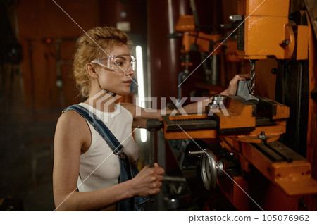Woman wearing safety protective goggles working on milling and drilling machine 105076962