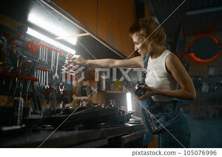 Young woman repairing spare part of motorcycle at workshop in evening 105076996
