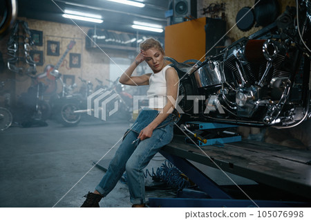 Attractive woman mechanic posing for camera at motorcycle garage Attractive woman mechanic posing for camera at motorcycle garage 105076998