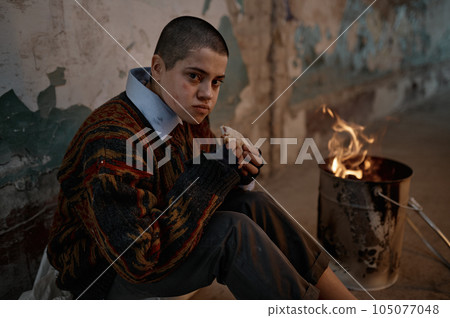 Poor homeless woman eating sandwich and warming at bonfire 105077048