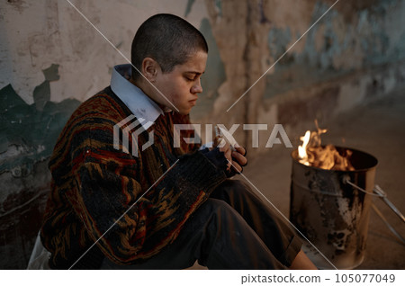 Poor homeless woman eating sandwich while warming at bonfire Poor homeless woman eating sandwich while warming at bonfire 105077049