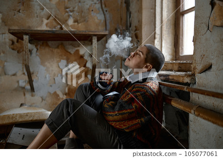 Homeless woman smoking sitting on room floor of abandoned house Homeless woman smoking sitting on room floor of abandoned house 105077061