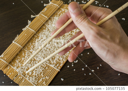 chopsticks in hand in the background of a sushi mat and scattered rice 105077135