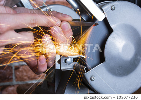 Knife sharpener and hand with blade on wooden table, closeup Knife sharpener and hand with blade on wooden table, closeup 105077230