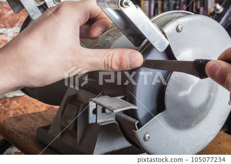 Knife sharpener and hand with blade on wooden table, closeup 105077234