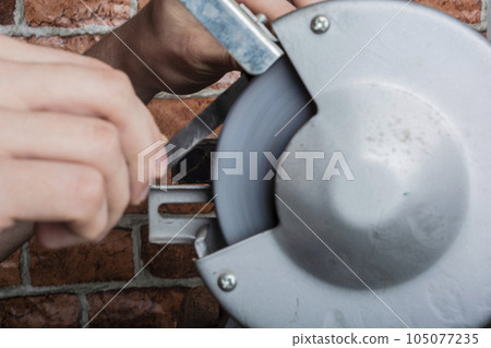 Knife sharpener and hand with blade on wooden table, closeup 105077235