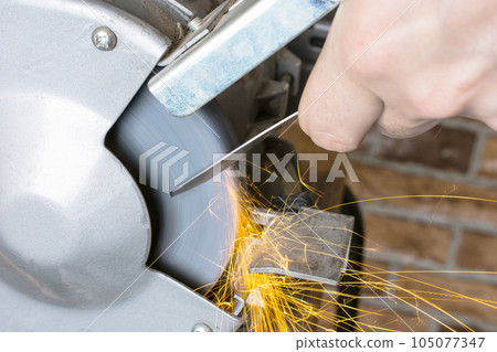 Knife sharpener and hand with blade on wooden table, closeup 105077347
