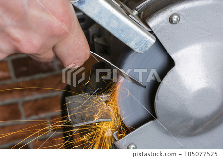 Knife sharpener and hand with blade on wooden table, closeup Knife sharpener and hand with blade on wooden table, closeup 105077525