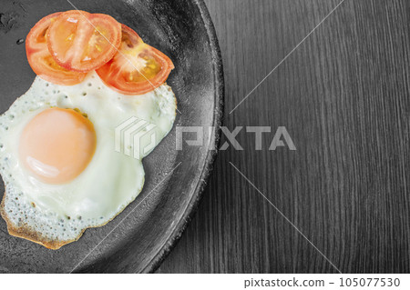 fried egg with tomatoes in a cast-iron frying pan on a wooden table 105077530