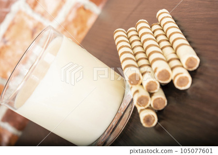 a glass of yogurt with a waffle straw on a black background and a brick wall 105077601