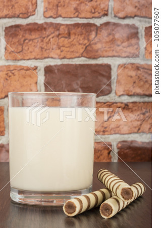 a glass of yogurt with a waffle straw on a black background and a brick wall 105077607