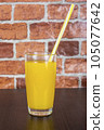Orange juice in a cup with a tube on a wooden table and a brick wall background 105077642