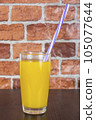 Orange juice in a cup with a tube on a wooden table and a brick wall background 105077644