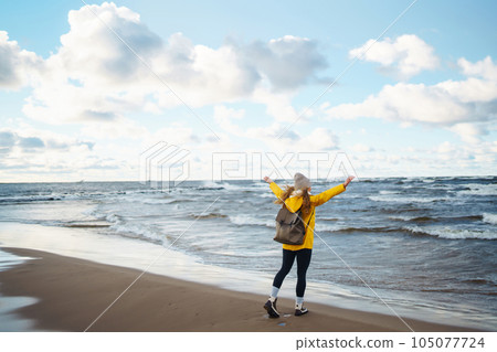 The girl tourist in a yellow jacket posing by the sea. Travelling, lifestyle, adventure. 105077724