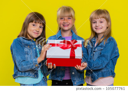 Three girls siblings friends presenting birthday gift box with red ribbon holidays sale discount 105077761