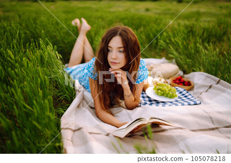 Young woman sits on a plaid with a book. Summer picnic in nature. Healthy food. Young woman sits on a plaid with a book. Summer picnic in nature. Healthy food. 105078218