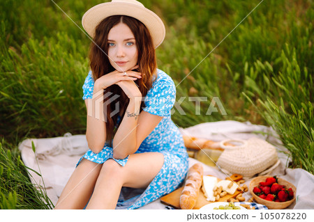 Young woman sits on a plaid with a book. Summer picnic in nature. Healthy food. 105078220