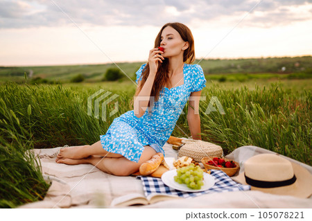 Young woman sits on a plaid with a book. Summer picnic in nature. Healthy food. Young woman sits on a plaid with a book. Summer picnic in nature. Healthy food. 105078221