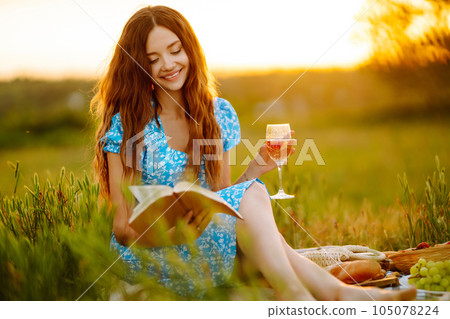Young woman sits on a plaid with a book. Summer picnic in nature. Healthy food. Young woman sits on a plaid with a book. Summer picnic in nature. Healthy food. 105078224