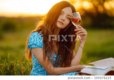 Young woman sits on a plaid with a book. Summer picnic in nature. Healthy food. 105078225