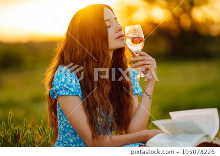 Young woman sits on a plaid with a book. Summer picnic in nature. Healthy food. Young woman sits on a plaid with a book. Summer picnic in nature. Healthy food. 105078226