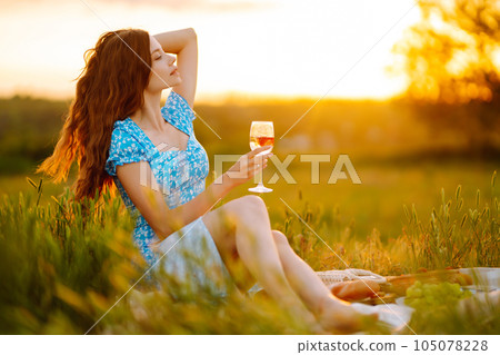 Young woman sits on a plaid with a book. Summer picnic in nature. Healthy food. 105078228