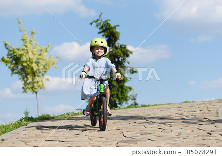 Happy small girl riding bike downhill in park with blue sky in background 105078291
