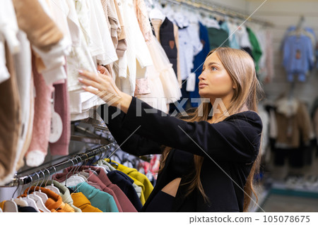 Pregnant woman choosing dress and bodysuits at clothing store. Mother doing shopping in baby shop. Baby clothes sale and pregnancy concept. 105078675